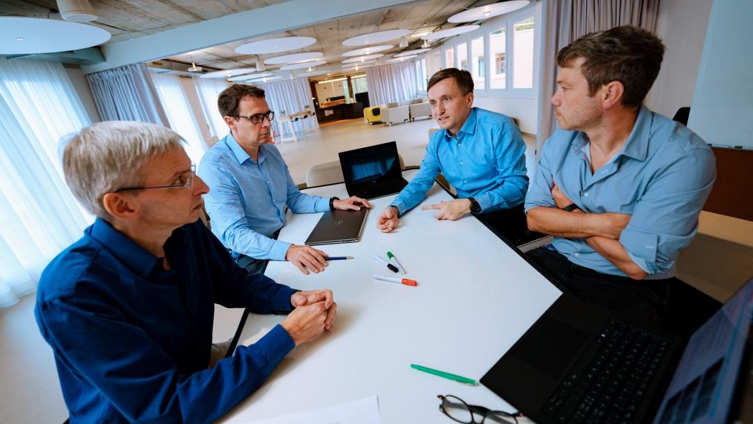 Adam Strzelecki and three colleagues are sitting at a table and are talking. There are laptops and pens on the table.
