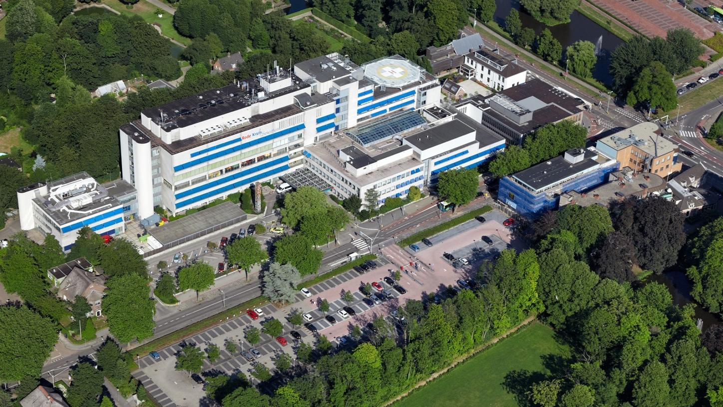 Wir sehen eine Luftaufnahme des “Rode Kruis” Krankenhauses im niederländischen Beverwijk. Das Gebäude liegt inmitten von Bäumen und Wiesen.  