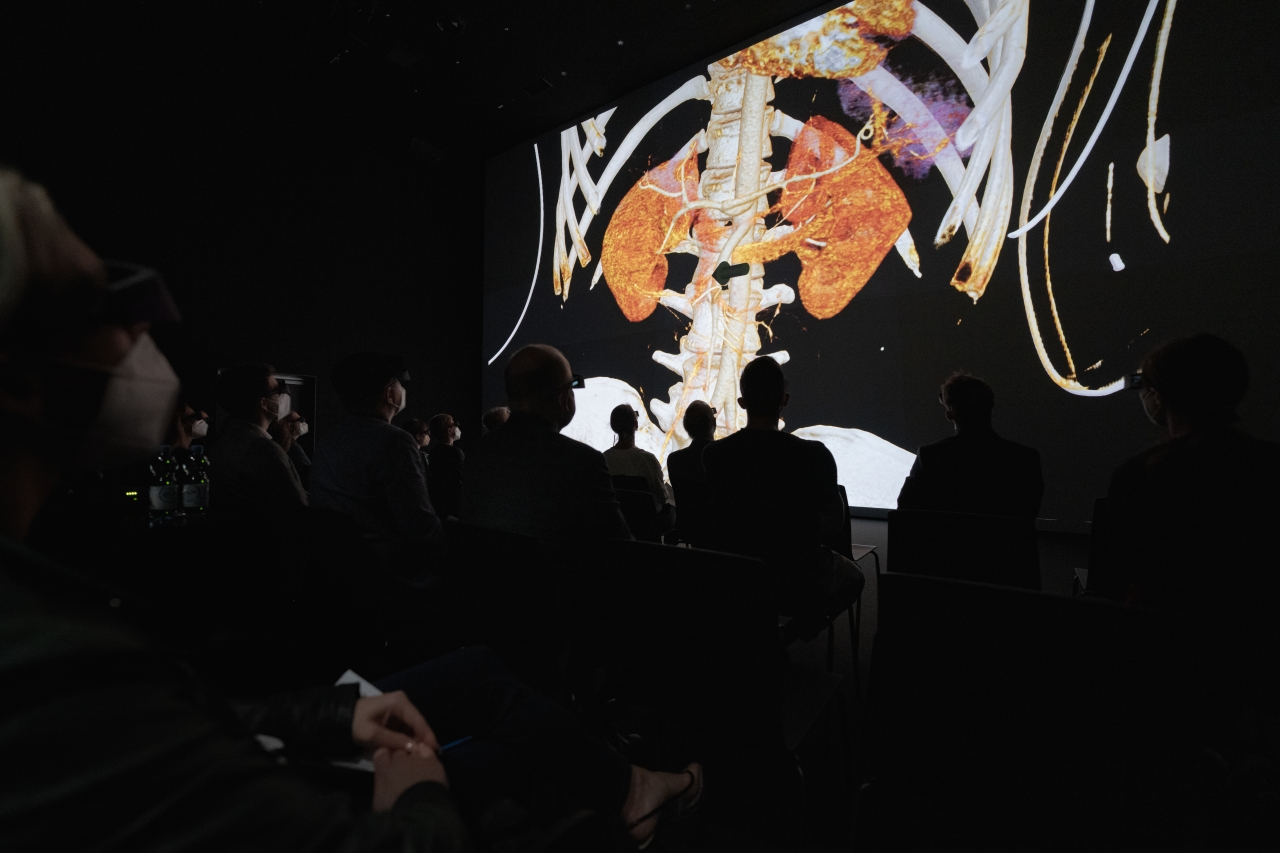 Photo of cinematic rendering displayed in the MedSpace at the University of Linz in Austria. It shows the audience, wearing VR glasses, sitting in front of a large screen watching a cinematic rendering of a human torso.